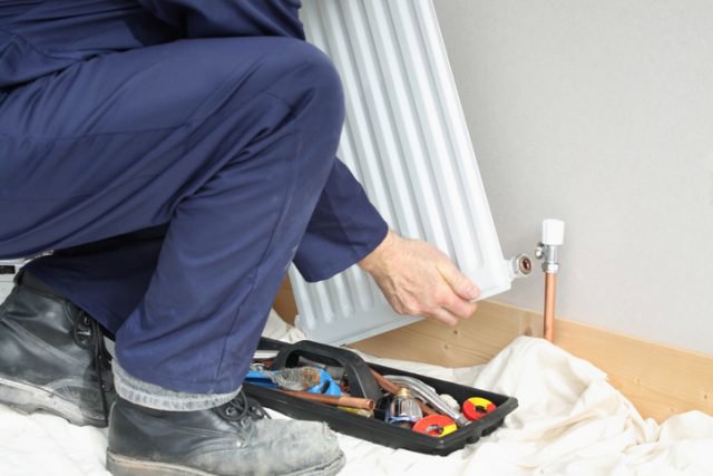 A technician installing or repairing a radiator with tools for Baker Heating & Cooling in Dayton, OH.