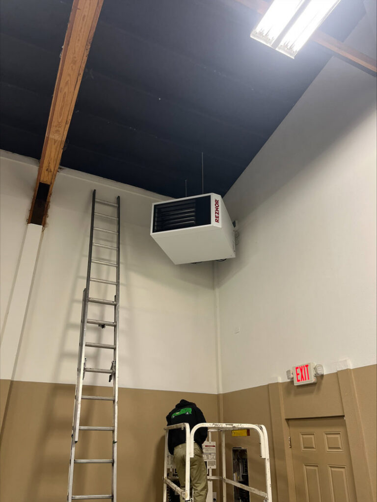 A Gagles Heating technician installing a Reznor unit heater in a commercial building in Salem, OR.