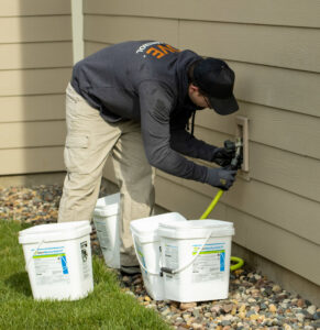 A technician installing a rodent bait station near a building's exterior for Pest Free Rochester in Rochester, MN.