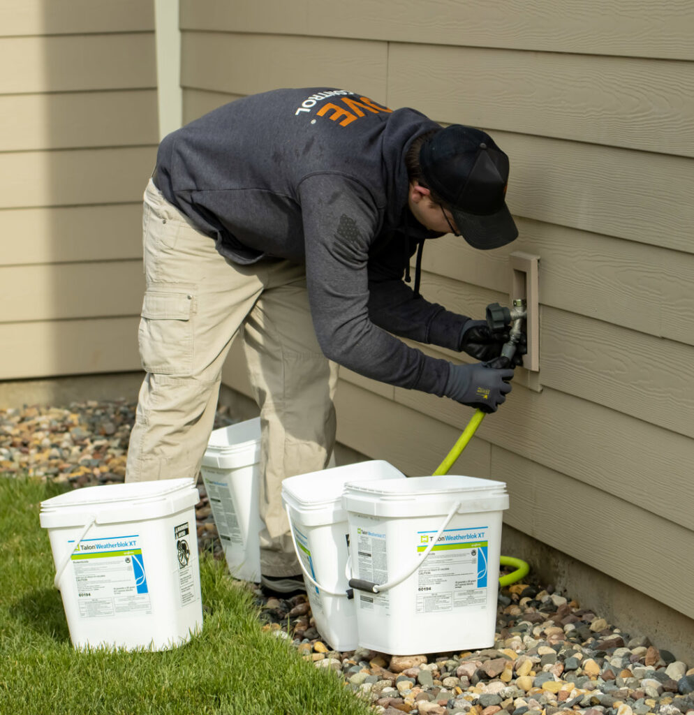 A technician installing a rodent bait station near a building's exterior for Pest Free Rochester in Rochester, MN.