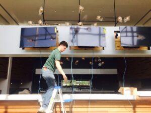 A technician on a ladder installing cabling for wall-mounted televisions, performed by D & D Cabling Solutions in Arlington, TX.