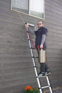 A technician from Eagle Eye Extermination on a ladder performing exterior pest treatment in Kalispell, MT.