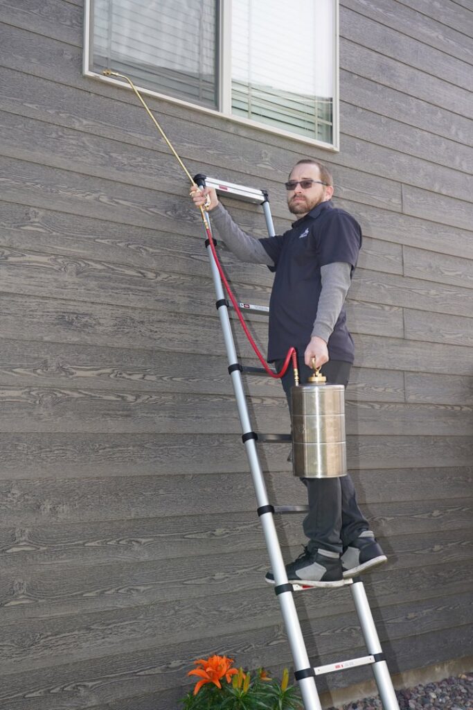 A technician from Eagle Eye Extermination on a ladder performing exterior pest treatment in Kalispell, MT.