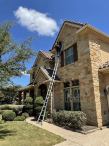 A technician on a ladder inspecting or treating a residential house for pests by CARE PEST PROS in Austin, TX.