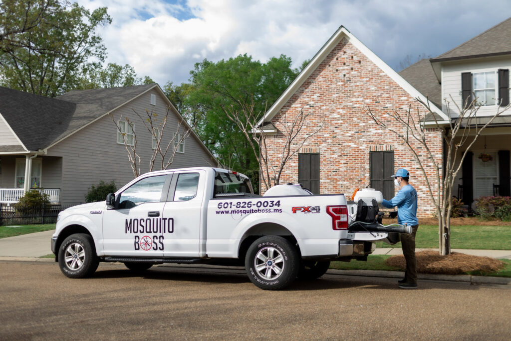A Mosquito Boss technician loading a backpack sprayer onto a service truck in Brandon, MS