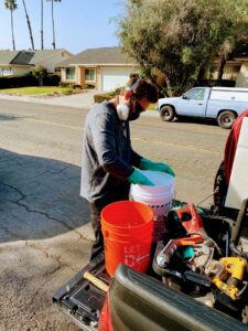 A technician wearing a respirator and gloves, mixing pesticides in buckets from a truck for United Termite Control in San Marcos, CA.