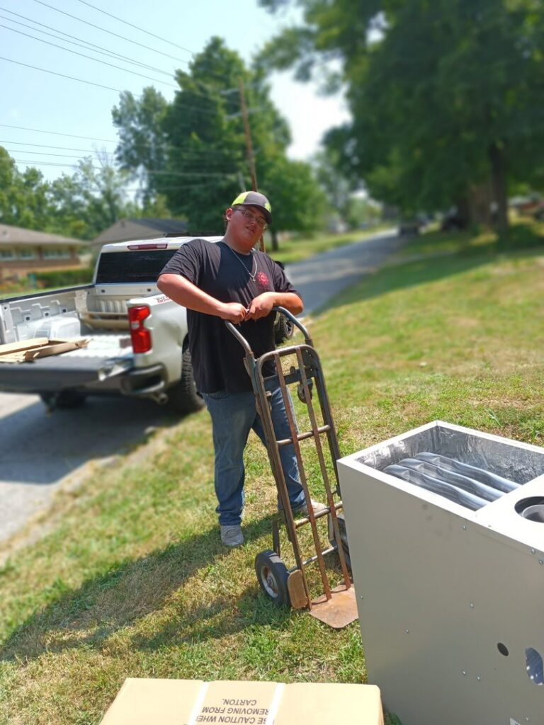 A TAS Mechanical Services technician moving an indoor HVAC furnace unit with a hand truck for installation or replacement in Kearney, MO.