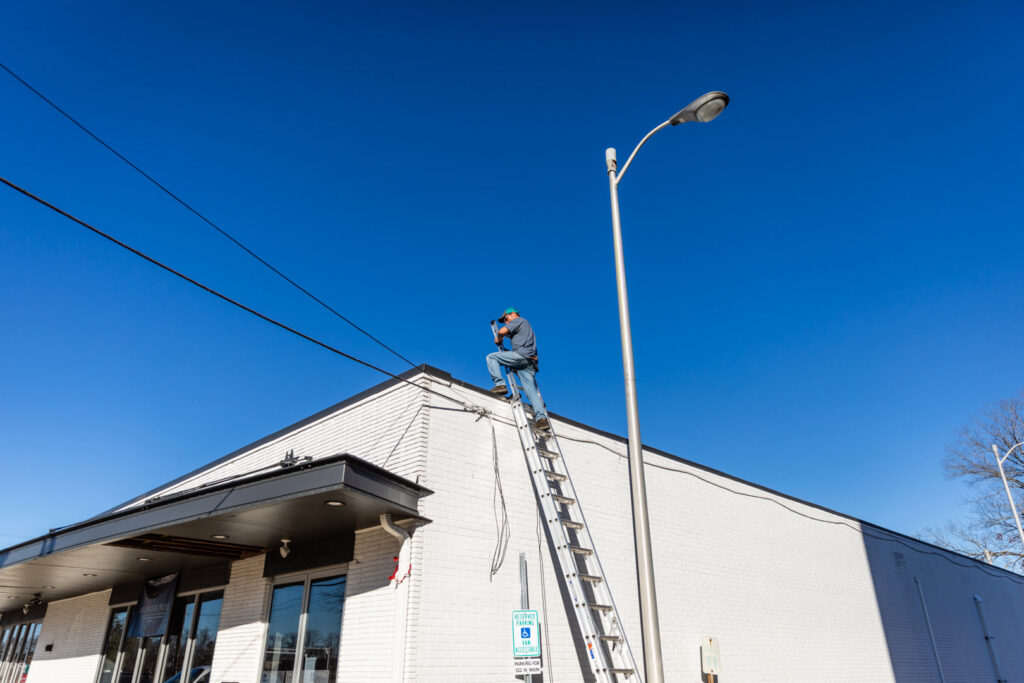 An HVAC technician on a ladder performing work on the exterior of a commercial building for Comfort Engineering Co Inc in Tupelo, MS