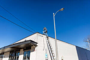 An HVAC technician on a ladder performing work on the exterior of a commercial building for Comfort Engineering Co Inc in Tupelo, MS