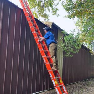 A pest control technician on a ladder inspecting the roofline of a commercial building for 1st Choice Pest Solutions in Eau Claire, WI.