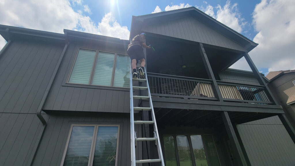 A KC Pest Experts technician on a ladder inspecting a roofline for pest or wildlife issues in Olathe, KS.