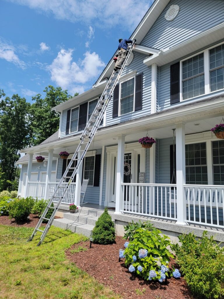 A technician on a ladder performing exclusion work on the side of a house for New England Wildlife Control in Salem, NH.