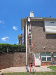 A technician on a tall ladder inspecting or working on the roof and gutter area of a house for Direct Pest Solutions Of Georgia, LLC in McDonough, GA.