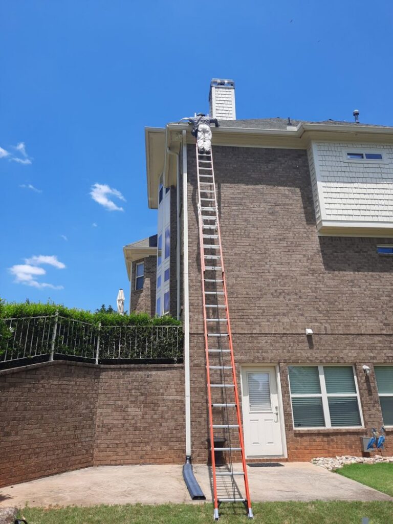 A technician on a tall ladder inspecting or working on the roof and gutter area of a house for Direct Pest Solutions Of Georgia, LLC in McDonough, GA.