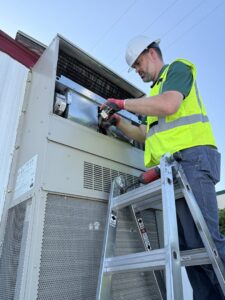 A Community Mechanical technician on a ladder servicing a commercial HVAC unit in Plano, TX.