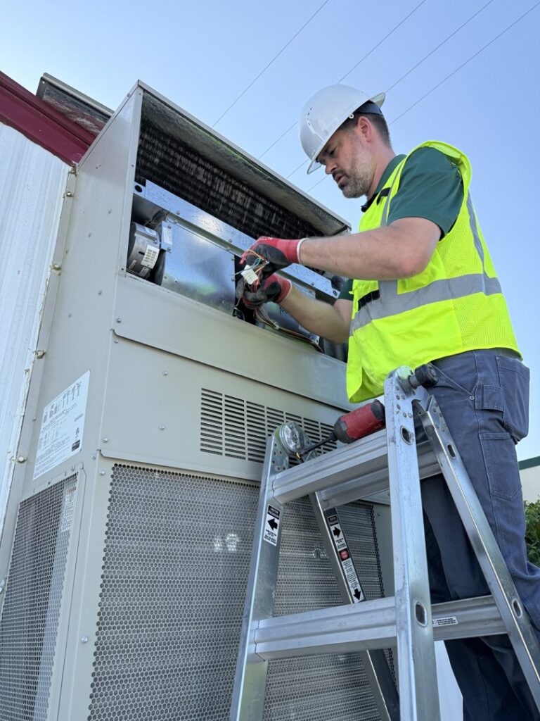 A Community Mechanical technician on a ladder servicing a commercial HVAC unit in Plano, TX.