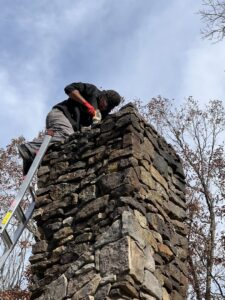 A technician on a ladder performing work on top of a stone chimney for Northwest Chimney in Bremerton, WA.