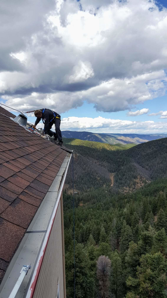 A technician on a roof, preparing for chimney work with safety gear, by Chimney Karma in Fort Collins, CO.