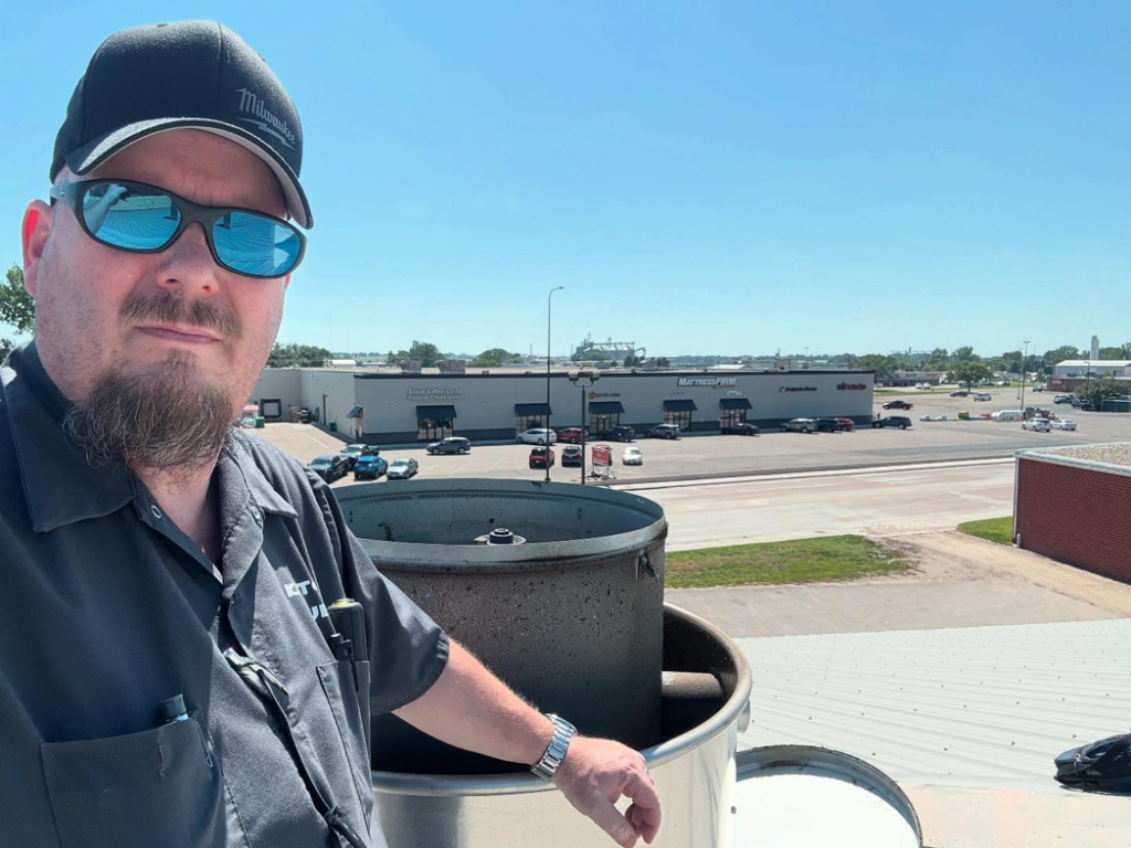 A technician from Commercial Kitchen Services, LLC of Watertown, SD, on a rooftop inspecting a large commercial HVAC unit.