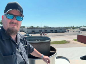 A technician from Commercial Kitchen Services, LLC of Watertown, SD, on a rooftop inspecting a large commercial HVAC unit.