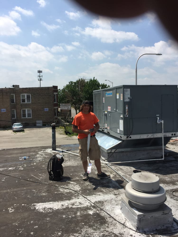 A technician standing on a rooftop next to a large commercial Daikin HVAC unit, performing service for Around The Town Heating and Cooling in Chicago, IL.
