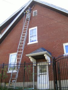 An ACS Animal Removal technician in Cincinnati, OH, on a tall ladder working on a house vent, likely for wildlife exclusion.