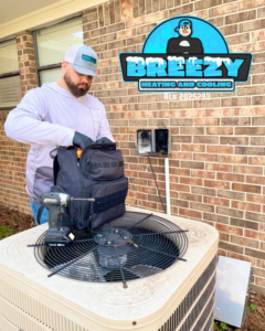 A Breezy Heating and Cooling technician performing service on an outdoor AC unit in Mobile, AL.