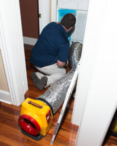 A technician performing duct cleaning or air quality service on an indoor HVAC vent for Thomas Service Company in Huntsville, AL
