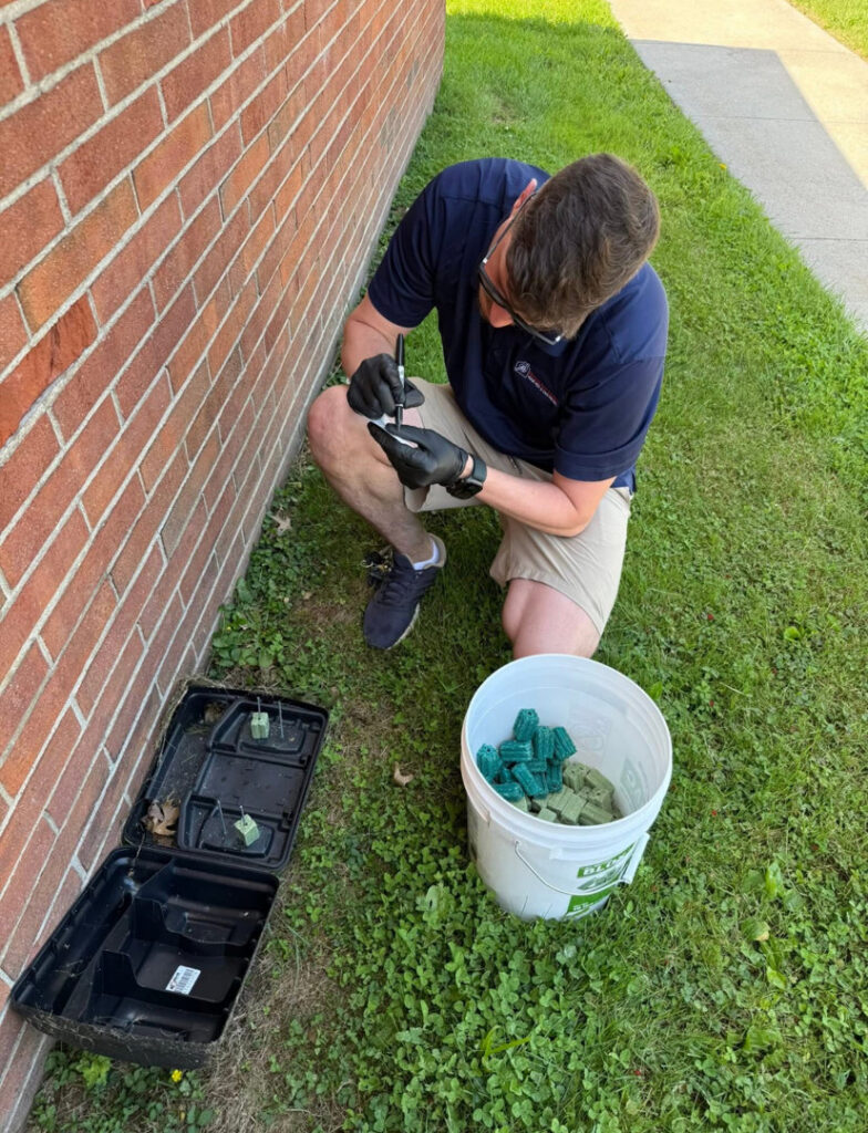 A pest control technician placing a rodent bait station next to a building at Devlins Pest Control in Reading, PA.