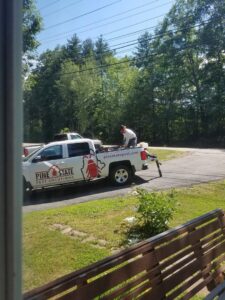 A pest control technician in protective gear preparing equipment on a Pine State Pest Solutions truck in Auburn, ME.
