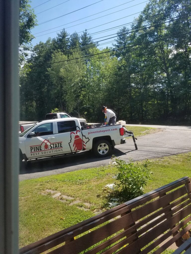 A pest control technician in protective gear preparing equipment on a Pine State Pest Solutions truck in Auburn, ME.