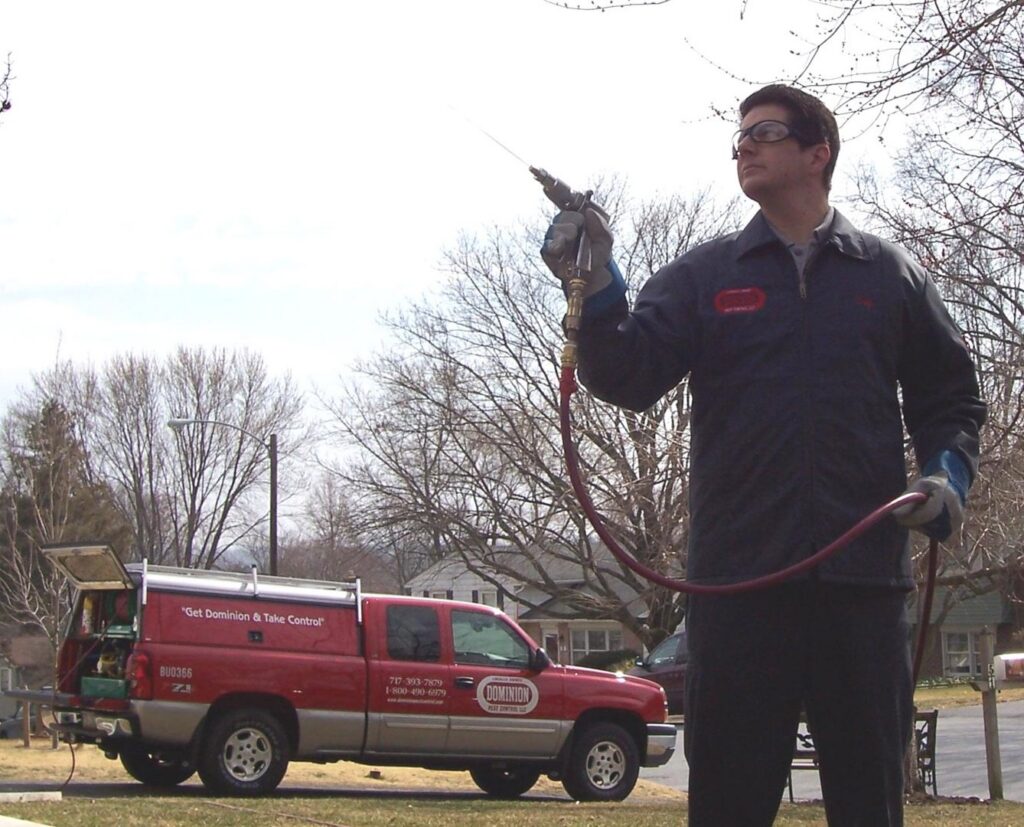 A Dominion Pest Control LLC technician preparing to spray, with a company truck in the background, in Lancaster, PA.