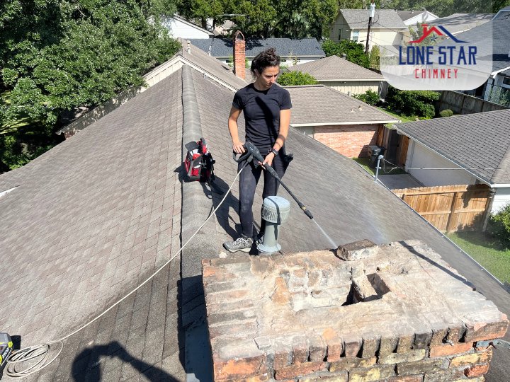 A Lone Star Chimney technician pressure washing a brick chimney on a residential roof in Houston, TX.