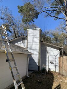A Lone Star Chimney technician pressure washing a brick chimney on a roof, with a rainbow effect, in Houston, TX.