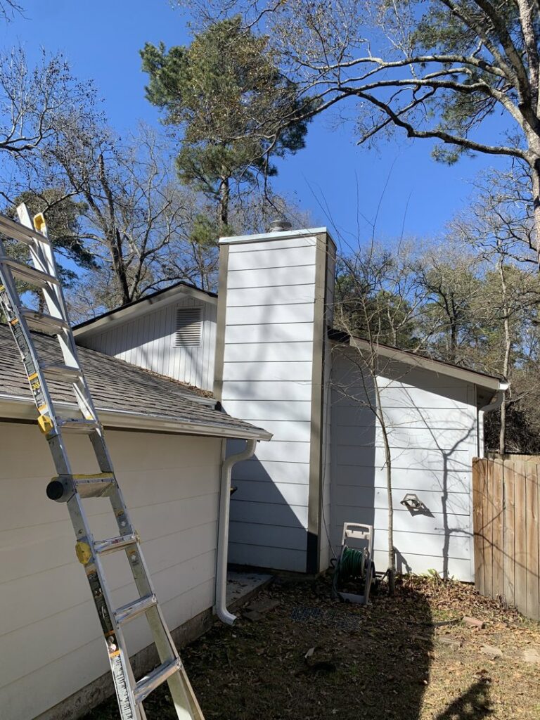 A Lone Star Chimney technician pressure washing a brick chimney on a roof, with a rainbow effect, in Houston, TX.