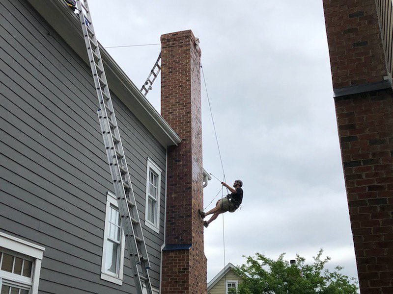 A technician from Emberstone Chimney Solutions rappelling down a tall brick chimney for inspection or repair in Charlotte, NC.
