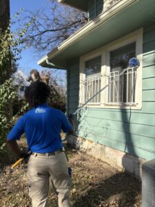 A Blue Beetle Pest Control technician removing cobwebs and nests from house eaves in Kansas City, MO.