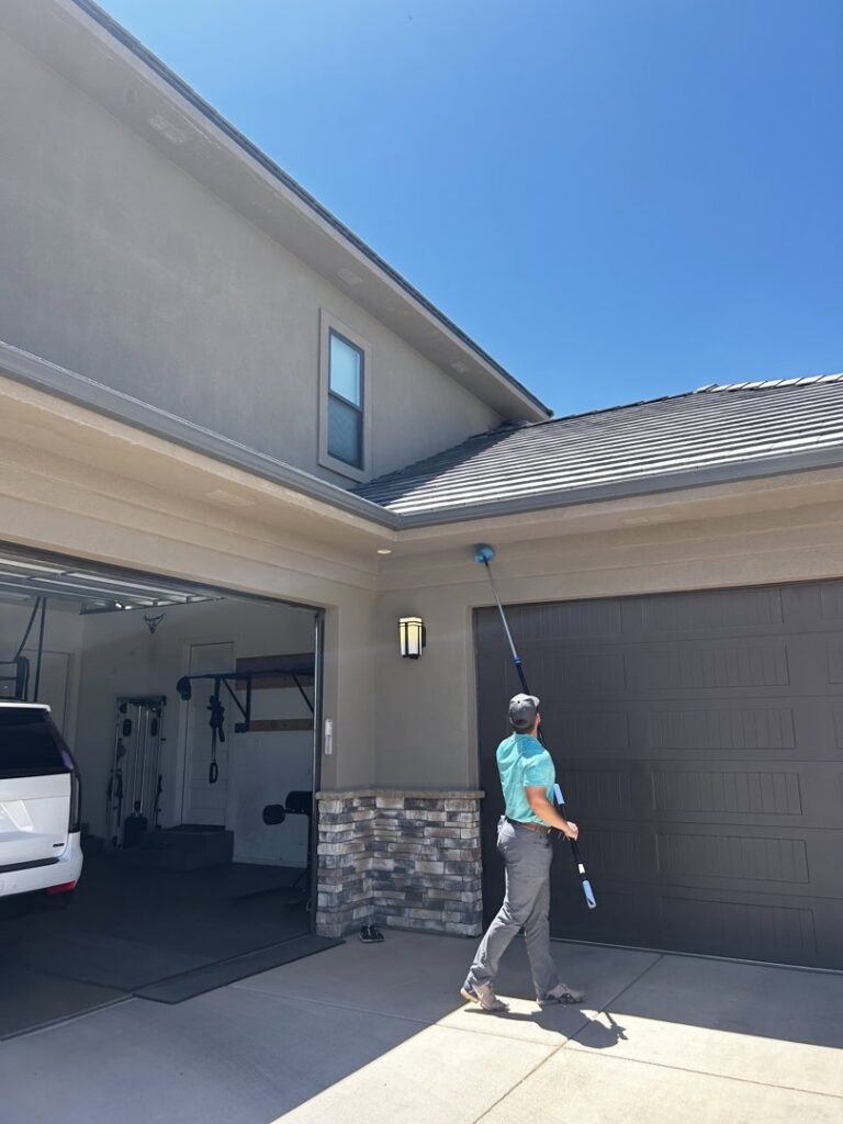 A Box Pest Control technician removing cobwebs and nests from under the eaves of a house in Farmington, NM.
