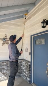 A Natrix Pest Control technician in Bakersfield, CA, removing cobwebs or wasp nests from under house eaves.