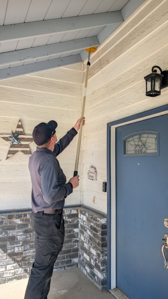 A Natrix Pest Control technician in Bakersfield, CA, removing cobwebs or wasp nests from under house eaves.
