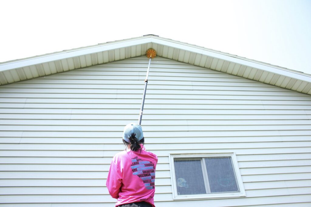 A Pest Badger technician removing cobwebs and nests from house eaves during a pest control service in Chippewa Falls, WI.
