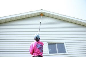 A Pest Badger technician removing cobwebs and nests from house eaves during a pest control service in Chippewa Falls, WI.