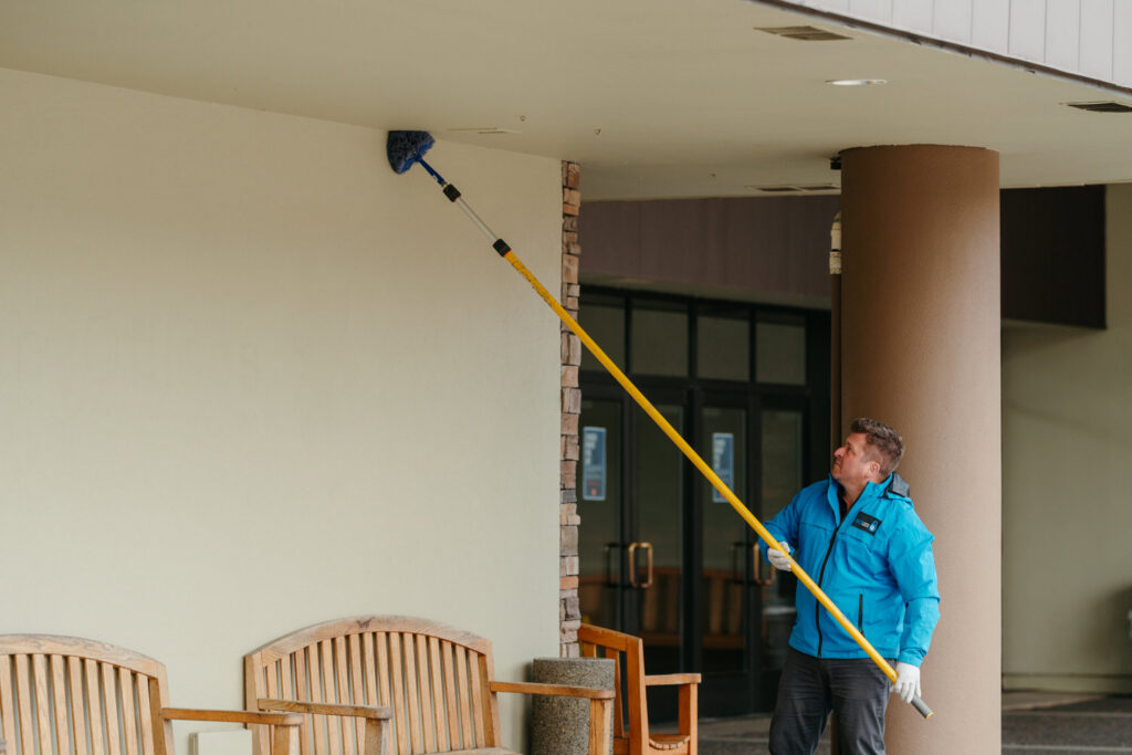 A Pest Lock, Inc. technician removing cobwebs and nests from a high eave as part of pest control in Vancouver, WA.