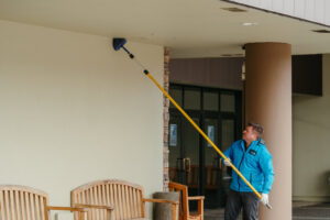 A Pest Lock, Inc. technician removing cobwebs and nests from a high eave as part of pest control in Vancouver, WA.