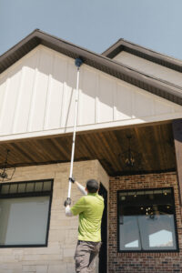 A pest control technician removing cobwebs and nests from the eaves of a house at Pure Pest Solutions in North Ogden, UT.