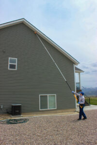 A Prompt Pest Solutions technician removing a nest or webs from the exterior of a house in Pocatello, ID.