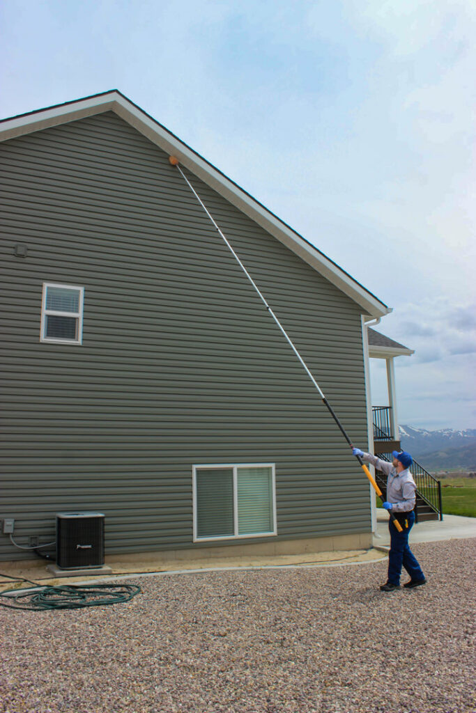 A Prompt Pest Solutions technician removing a nest or webs from the exterior of a house in Pocatello, ID.