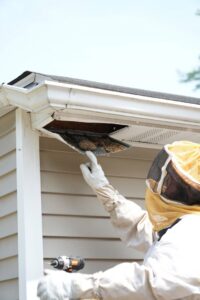 A pest control technician in a bee suit removing a nest from a soffit or fascia for Complete Pest Solutions of Canton in North Canton, OH.