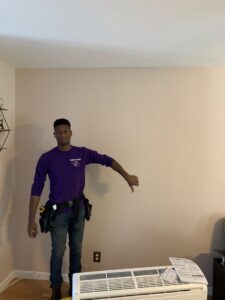A Hyper Fusion Heating & Cooling technician giving a thumbs down next to an old mini-split indoor unit, indicating replacement or removal in Waterbury, CT.