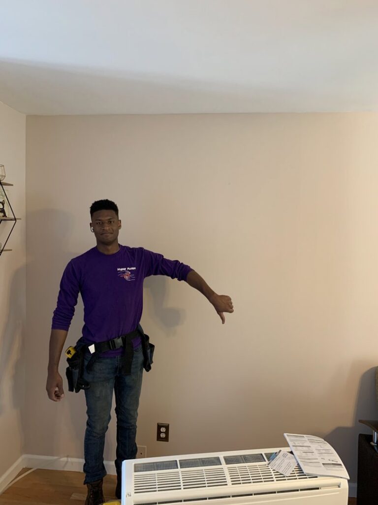 A Hyper Fusion Heating & Cooling technician giving a thumbs down next to an old mini-split indoor unit, indicating replacement or removal in Waterbury, CT.